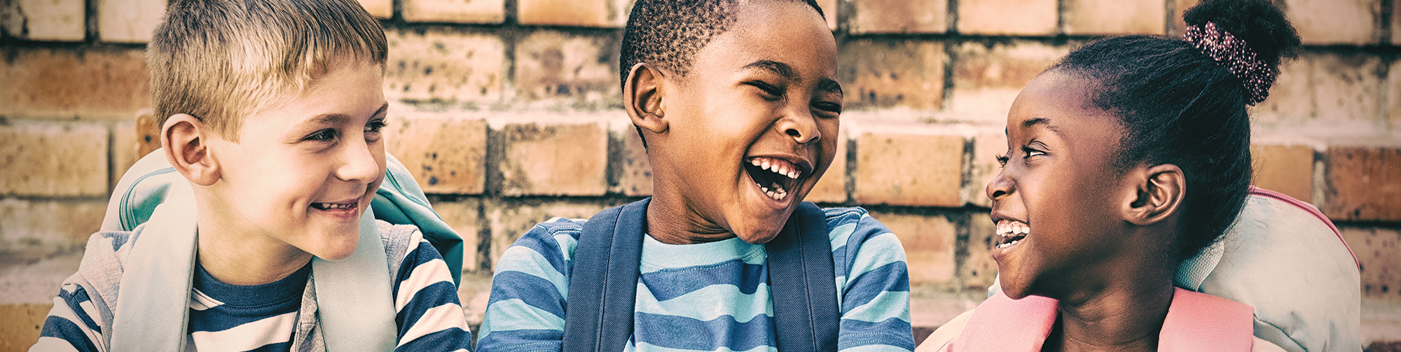 Three young diverse children laughing with each other